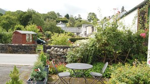 Un patio jardín con mesa y sillas, rodeado de abundante vegetación y plantas en flor.