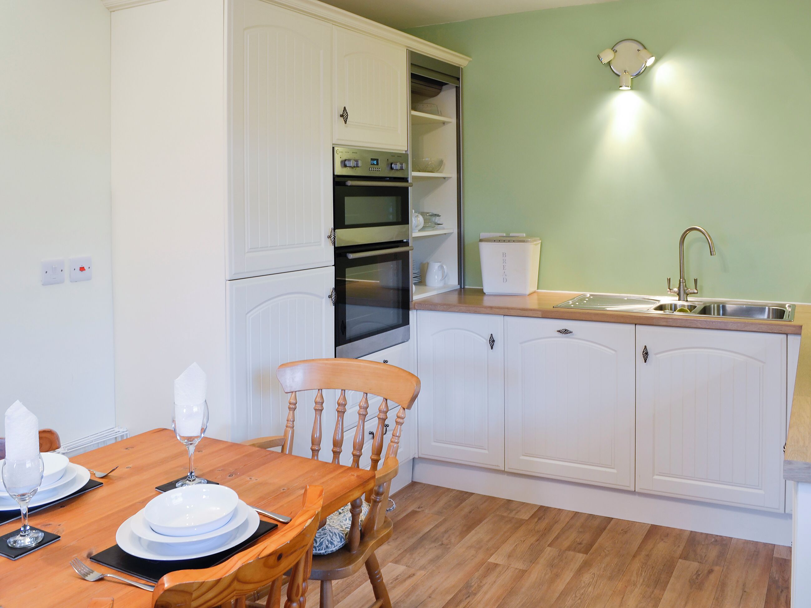 A kitchen with white cabinets, a wooden dining table set for four, and a built-in oven.