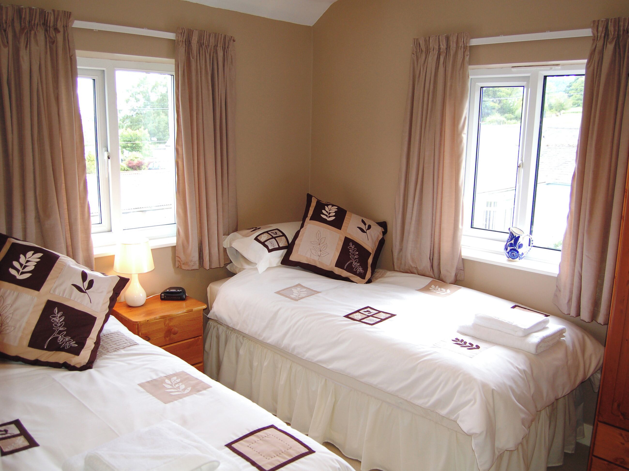 A hotel room with two beds, beige walls, and a window with curtains.