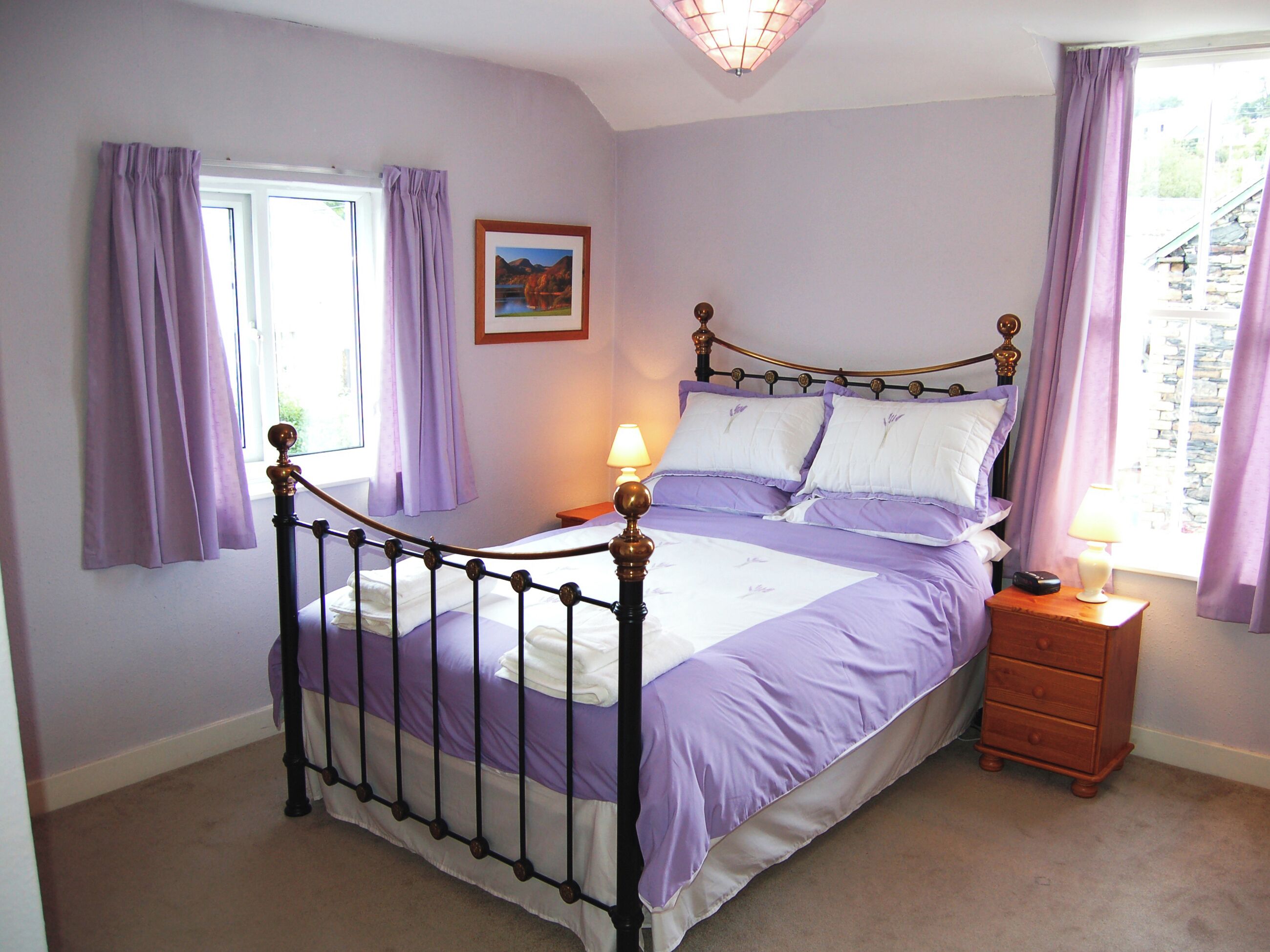 A bedroom with a four-poster bed, a bedside table with a lamp, and a window with purple curtains.