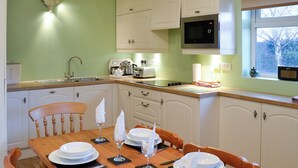 Una cocina con una mesa de comedor para cuatro, armarios blancos, un microondas y una ventana con vistas a árboles.