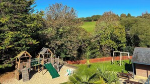 A playground with a slide and climbing wall, surrounded by trees and a grassy field. - Villa Gallery - 27074 (Carnon Downs, near Truro)