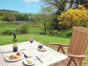 Una mesa al aire libre con una botella de vino, copas, platos con comida y una silla.