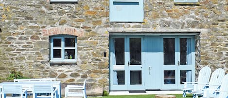 A stone building with a blue door and windows, outdoor seating with chairs and tables, and a well-maintained lawn.