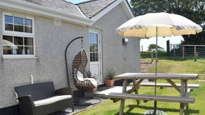 A patio area with a hanging chair, a table, and an umbrella. - Cefn Helyg Bach - 28453 (Cemaes Bay)
