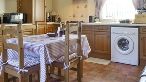 A compact kitchen with wooden cabinets, a microwave, a stove, and a washing machine. - Cefn Helyg Bach - 28453 (Cemaes Bay)