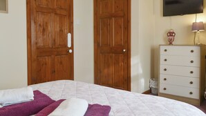 A bedroom with a bed, two wooden doors, a dresser, and a television on the wall. - Cefn Helyg Bach - 28453 (Cemaes Bay)