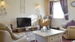 A living room with a TV, sofa, and a small table with remote controls. - Cefn Helyg Bach - 28453 (Cemaes Bay)