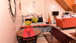 A compact room with a bed, a sofa, a TV, and a dining area with a table and chairs. - Sherry Homes Zuri Studio (Nairobi)