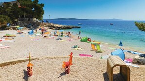 Ein Strand mit badenden Personen, bunten Sonnenschirmen und einer hölzernen Bank.