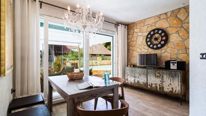 Ein Essbereich mit Tisch, Stühlen, einer Chandelierleuchte, einer Steinwand, einer Dartscheibe, einem Fernseher und einem rustikalen Schrank.
