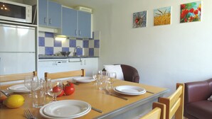 A dining area with a wooden table set for four, including plates, glasses, and cutlery. There are two chairs, a microwave, and a kettle on the counter. - VVF La Salvetat sur Agoût (La Salvetat-sur-Agout)