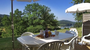 A table set outdoors with a view of a lake and hills, surrounded by white chairs and a wooden structure. - VVF La Salvetat sur Agoût (La Salvetat-sur-Agout)