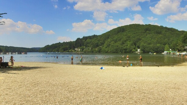 A beach with people swimming and walking along the shore, a forested hill in the background, and a clear sky. - VVF La Salvetat sur Agoût (La Salvetat-sur-Agout)