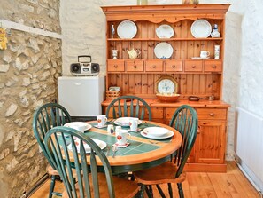 A dining area with a round table, four chairs, a wooden cabinet with dishes, a radio, and a refrigerator.