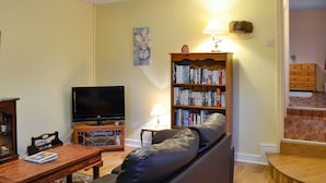 Un salon avec un canapé en cuir, une table basse en bois, un téléviseur, une bibliothèque et une lampe.