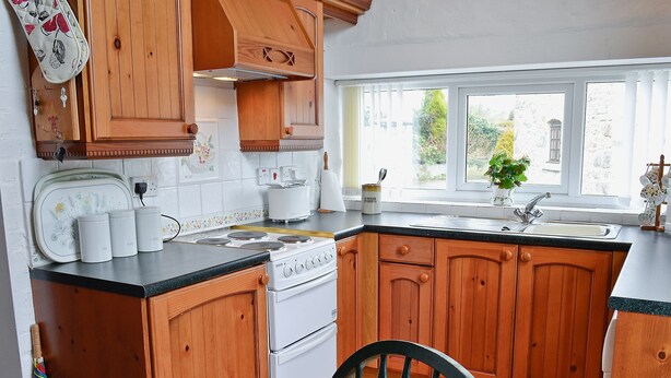 Une cuisine avec des meubles de rangement en bois, une cuisinière, un évier et une fenêtre donnant sur un paysage verdoyant.