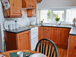 Una cocina con armarios de madera, estufa, lavabo y ventana con vista a follaje exterior.