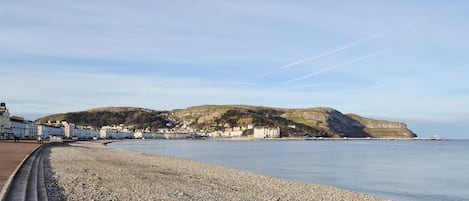 Una playa de guijarros con edificios al fondo y una colina.