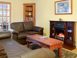 Una sala de estar con un sofá de cuero marrón, una mesa de centro de madera, una chimenea y un mueble de madera con estantes.