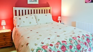 Une chambre avec un mur rouge, une tête de lit en bois, une literie à motifs floraux, deux lampes de chevet et un tableau encadré au-dessus du lit.