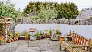 Une terrasse en pierre avec un banc en bois et différentes plantes en pot.