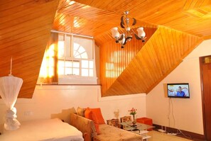 A cozy room with a sloped ceiling, a bed, a sofa, a TV, and a window with curtains.