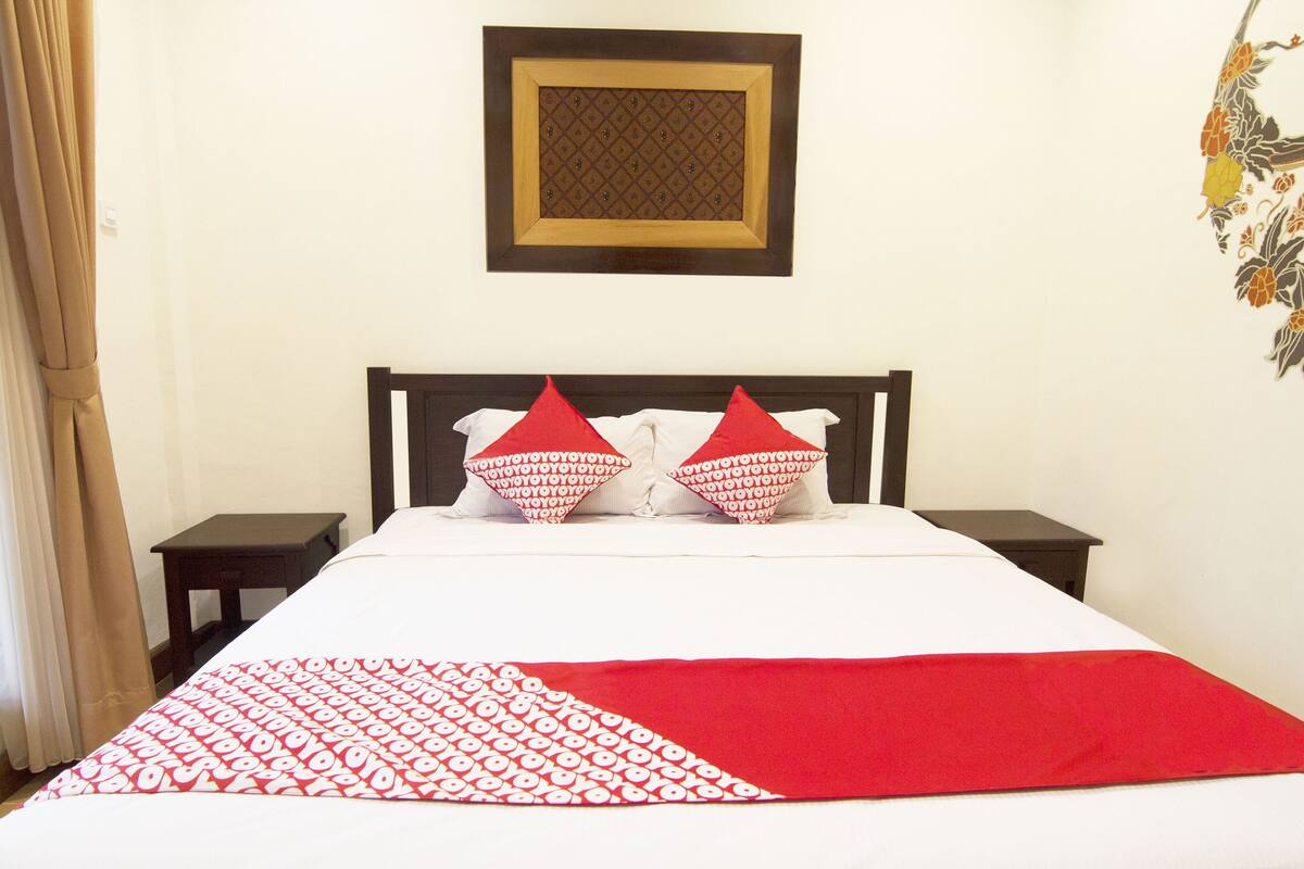 Ein Hotelzimmer mit einem Bett, zwei Nachttischen, einer rot-weißen Bettdecke und einem an der Wand hängenden Bilderrahmen.