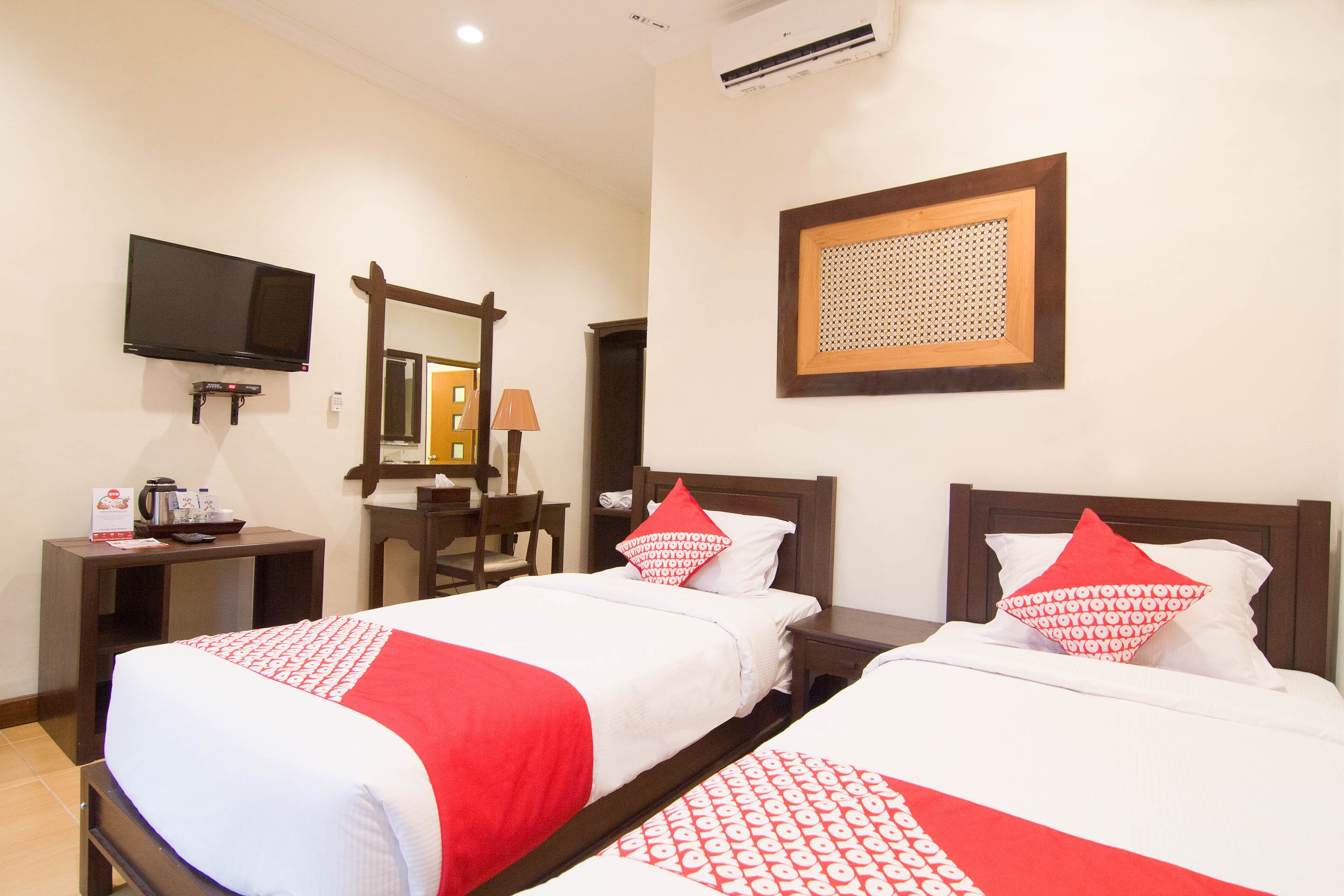A hotel room with two beds, a TV, a desk with a lamp, and a mirror.