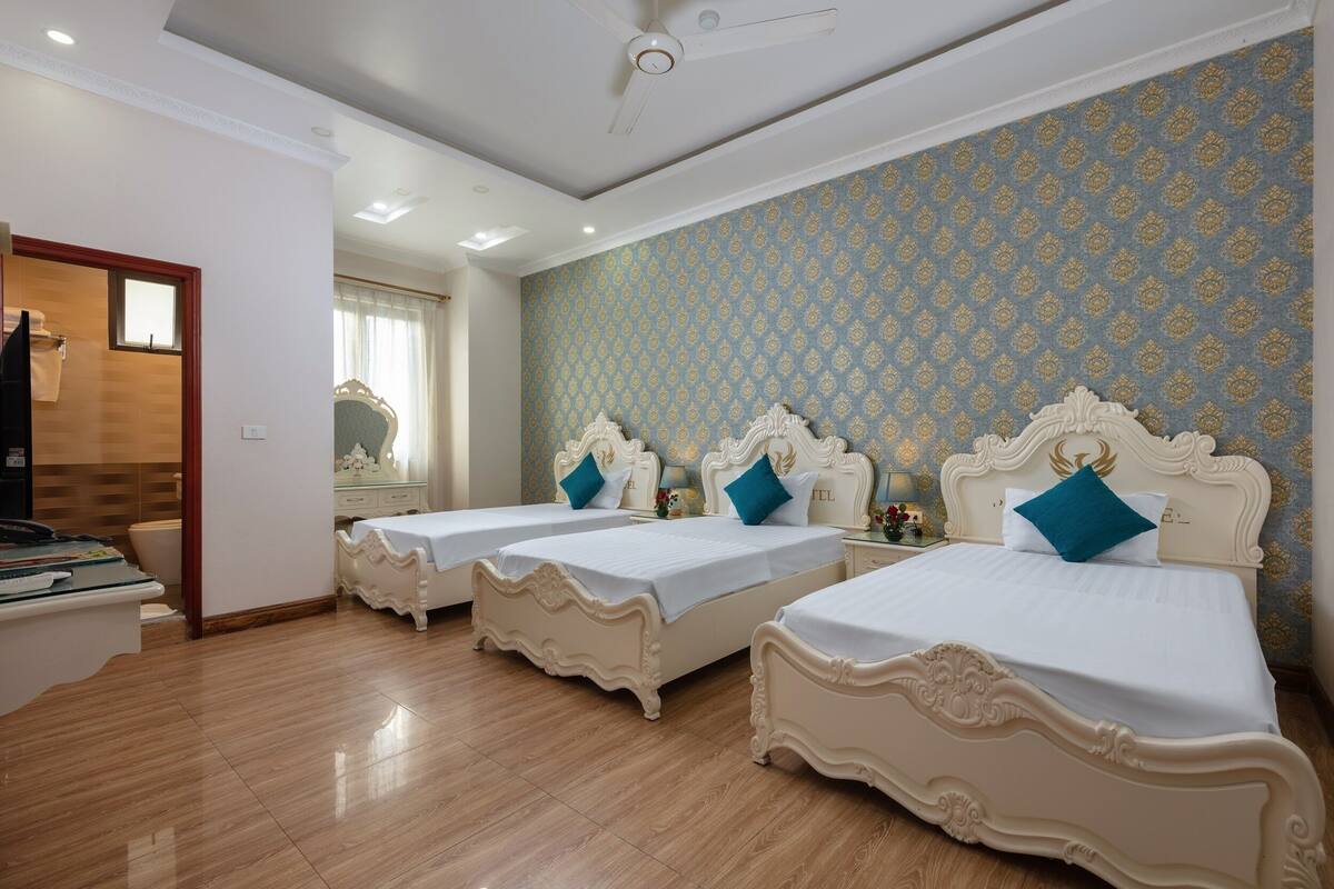 A hotel room with three beds, a ceiling fan, and a bathroom visible through an open door.