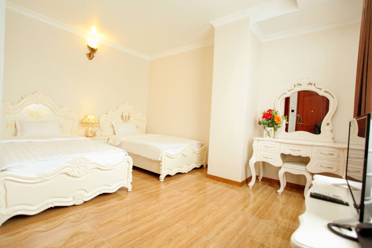 A hotel room with a large bed, a smaller bed, a vanity with a mirror, and a television.