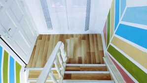 Una escalera de madera con barandillas blancas que conduce a una habitación con una puerta blanca y cortinas estampadas.
