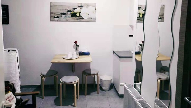 Una habitación pequeña y moderna con una mesa de madera, dos sillas, un bote de basura y un cuadro en la pared.