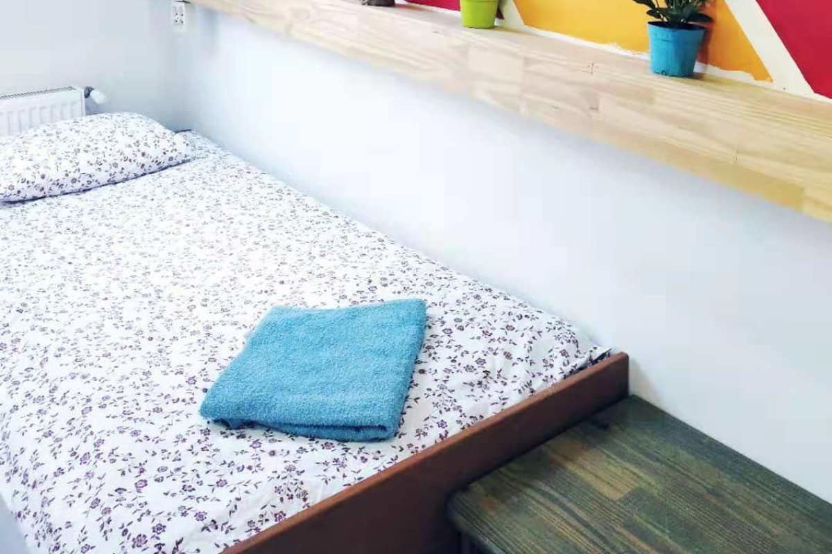 Ein Schlafzimmer mit schrägen Wänden, einem Bett mit Blumendecke, einem blauen Handtuch und einem Regal mit Blumentöpfen.