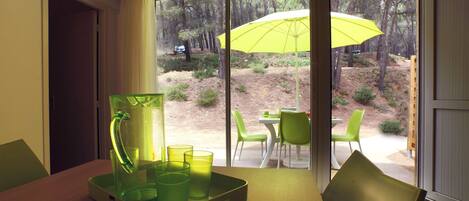 Una habitación con una mesa preparada para dos personas, una silla verde y un paraguas amarillo en el exterior.