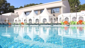 A swimming pool with clear blue water, surrounded by lounge chairs and umbrellas, and a building with multiple windows and a white facade. - VVF Montagnac Hérault (Montagnac)