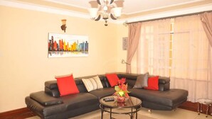 Ein Wohnzimmer mit einem schwarzen Ecksofa, einem Glastisch und einem Stadtbild an der Wand.