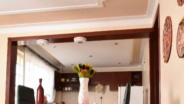Ein Essbereich mit einem Tisch, der mit einer roten Tischdecke bedeckt ist, einer Vase mit Blumen und einer Küche im Hintergrund.