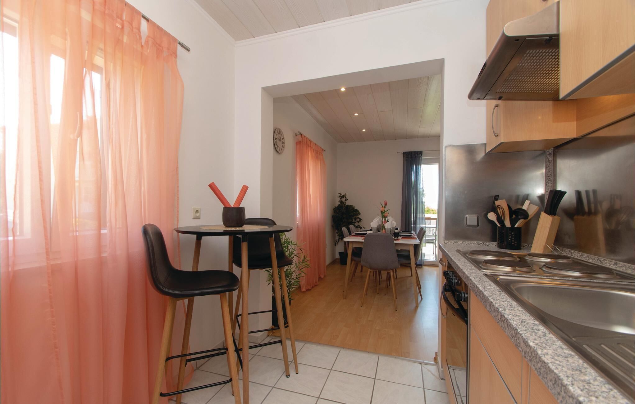 A modern kitchen with a stainless steel sink, wooden cabinets, and a dining area with a table and chairs.