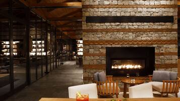 A cozy lounge area with a stone fireplace, wooden furniture, and a glass display case with books.