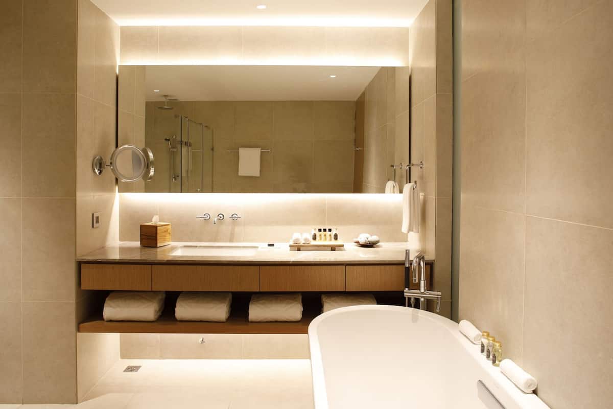 A modern bathroom with a large mirror, a bathtub, a vanity with a sink, and a towel rack.