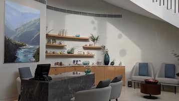 Interior moderno com uma receção de mármore, cadeiras cinzentas, um armário de madeira com prateleiras e um grande quadro de paisagem.