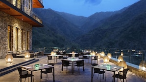 An outdoor dining area with tables and chairs, surrounded by stone walls and overlooking a valley. - Taj Rishikesh Resort & Spa, Uttarakhand (Narendranagar)