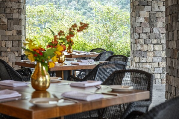 Ein Restaurant mit Steinsäulen und Blick auf Grünflächen. Tische sind gedeckt mit Geschirr und Besteck.