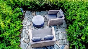 A garden with a stone patio and outdoor seating, surrounded by lush greenery and a view of a mountain. - Taj Rishikesh Resort & Spa, Uttarakhand (Narendranagar)