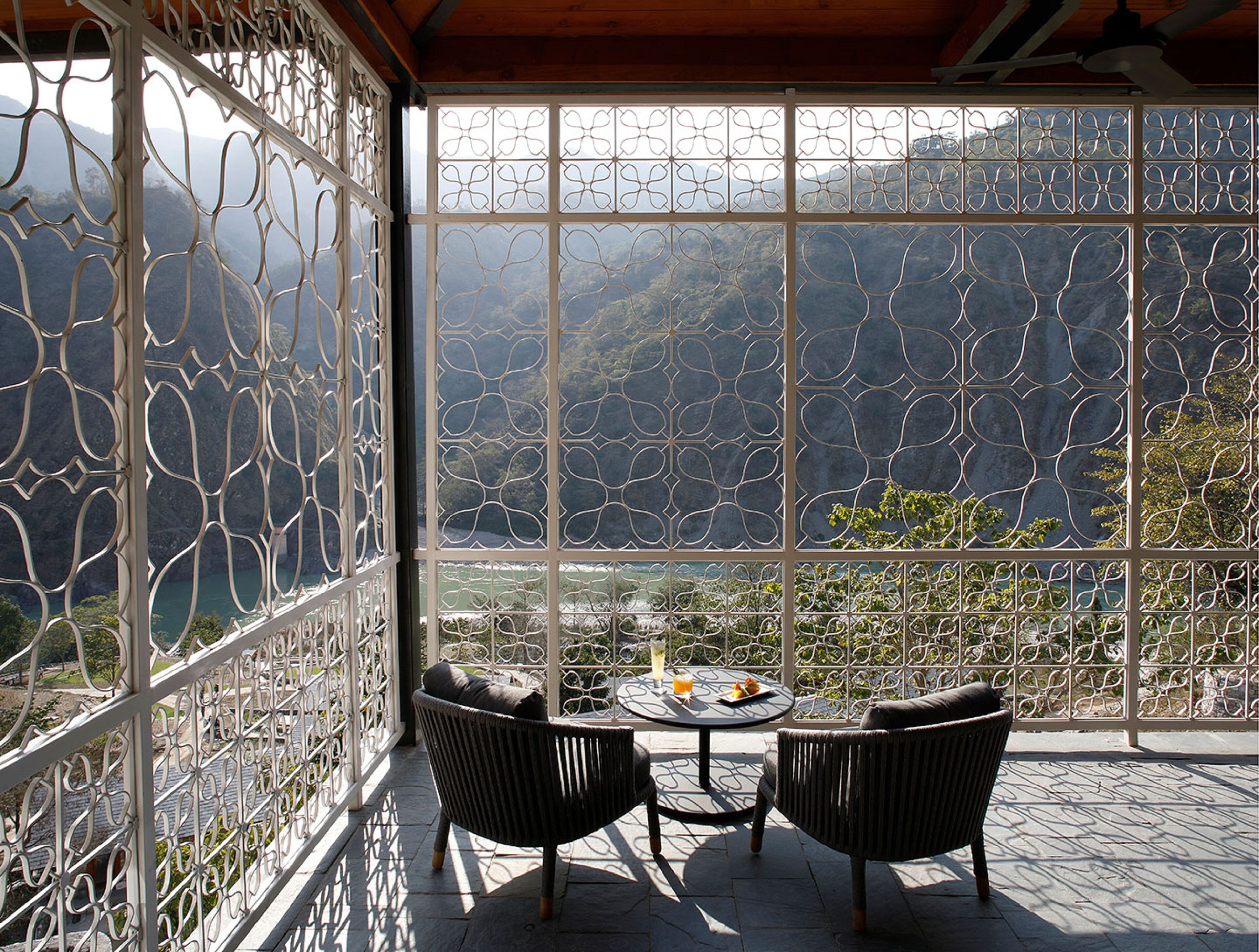 A balcony with a view of mountains, two wicker chairs, and a table with a drink.