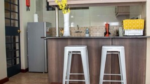 A kitchen with a wooden countertop, two white bar stools, a refrigerator, and a yellow flower vase.