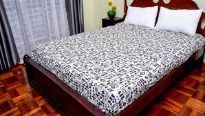 A neatly made bed with a patterned bedspread, a wooden headboard, and a nightstand with a vase of flowers.