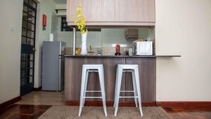 A kitchen with a wooden countertop, two white bar stools, a refrigerator, and a vase with yellow flowers.