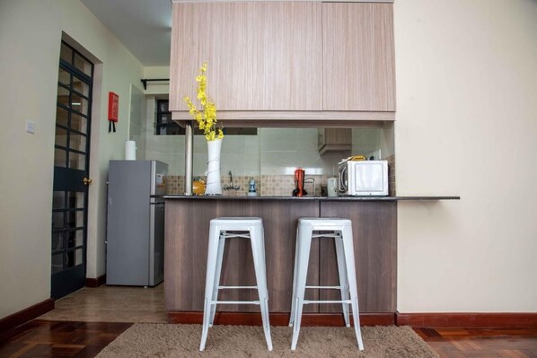 A kitchen with a wooden countertop, two white bar stools, a refrigerator, and a vase with yellow flowers.